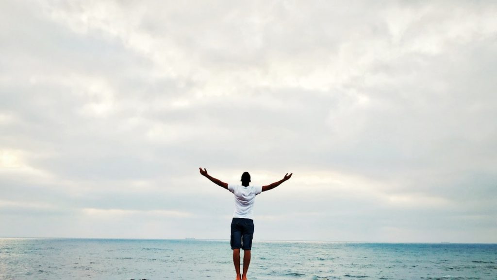 man raising hands standing near seashore during daytime