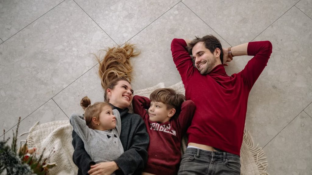 Smiling family of four lying on a blanket, sharing happiness and love indoors.